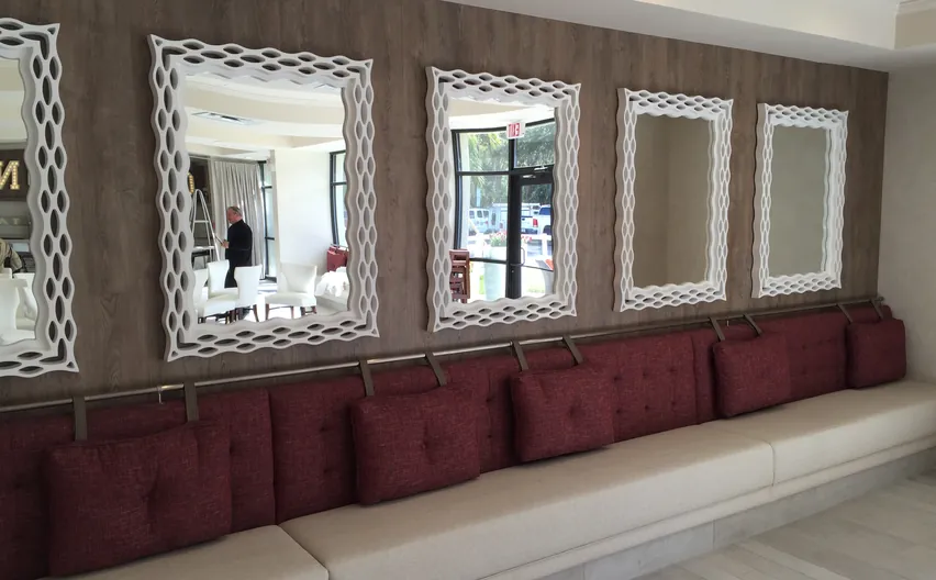 A long upholstered banquette with red cushions under a row of white framed mirrors