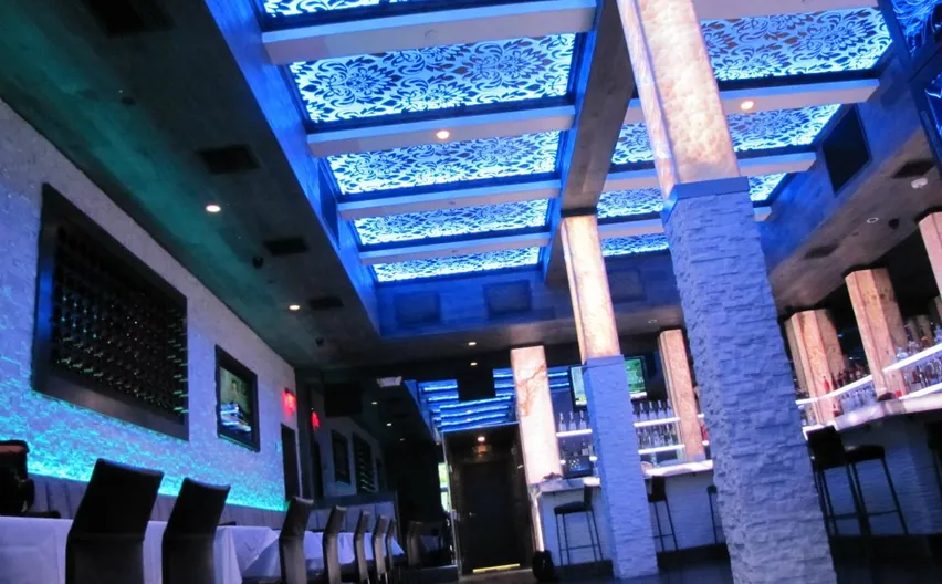 A bar and restaurant interior with blue-lit decorative ceiling panels and stone-clad columns